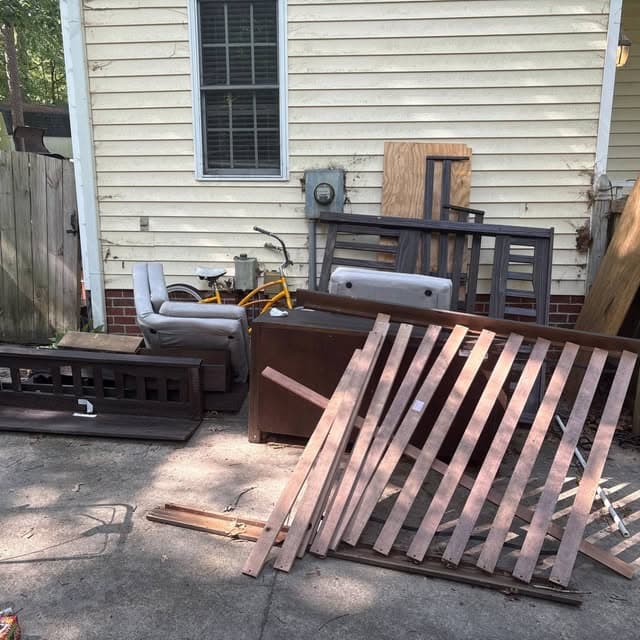 Furniture and scrap wood piled in a backyard before a property cleanout in Pitt County, NC